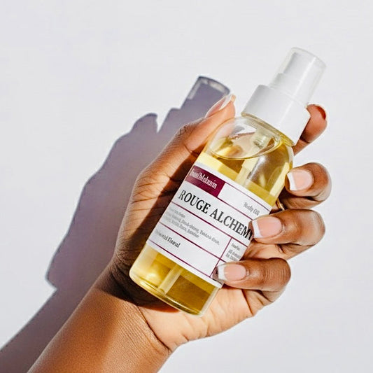 Hand holding a bottle of 'Rouge Alchemy' body oil by SeoulMelanin against a light background